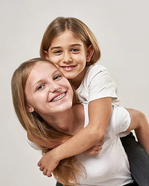 young girl with braces holding her younger sister piggyback