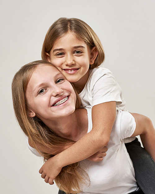 young girl with braces holding her younger sister piggyback